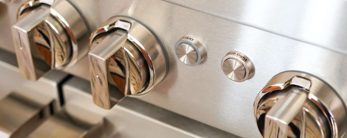 Closeup of the front of a JennAir Range. There are three knobs and two buttons.