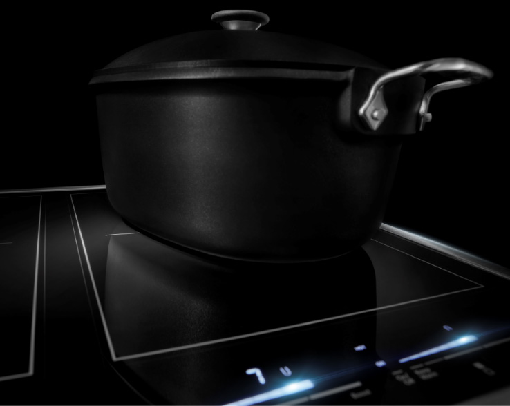 On a JennAir Ceramic Cooktop is a lidded black pot. Some of the controls are lit white