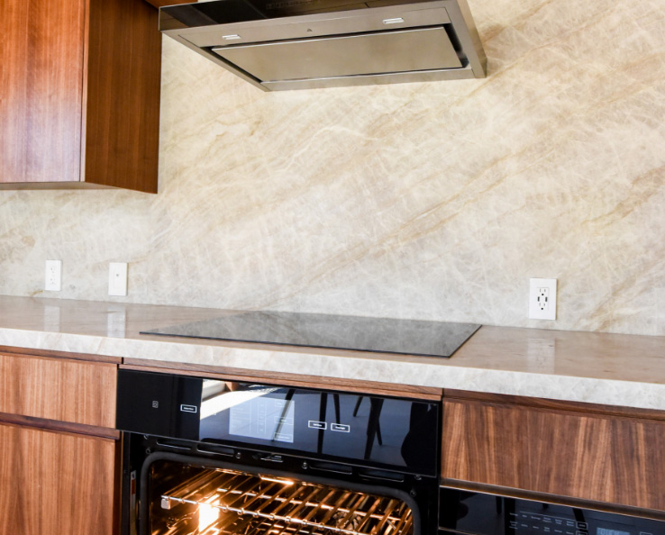 A kitchen with a JennAir Ceramic Cooktop below a JennAir Over-the-Range Hood Vent. Below the cooktop is a JennAir Oven with the door open.