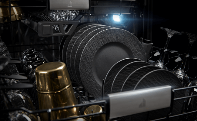  L'intérieur d’un lave-vaisselle JennAir. Un panier est rempli de verres, tasses, verres à vin, grandes et petites assiettes.