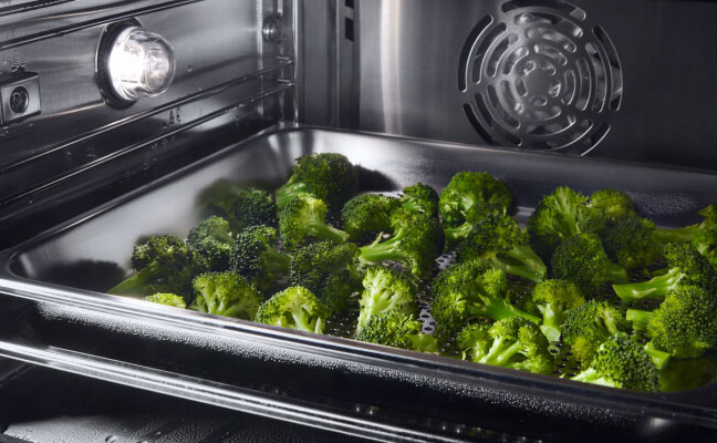 Broccoli bakes in a roasting pan inside an oven. 