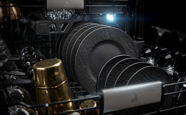  L'intérieur d’un lave-vaisselle JennAir. Un panier est rempli de verres, tasses, verres à vin, grandes et petites assiettes.