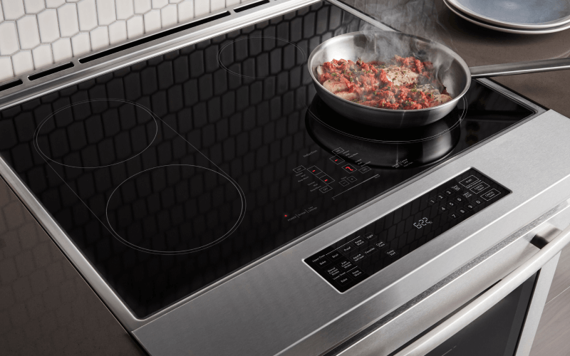 A JennAir induction range. On a burner is a pan filled with food. Steam is coming out of the pan.