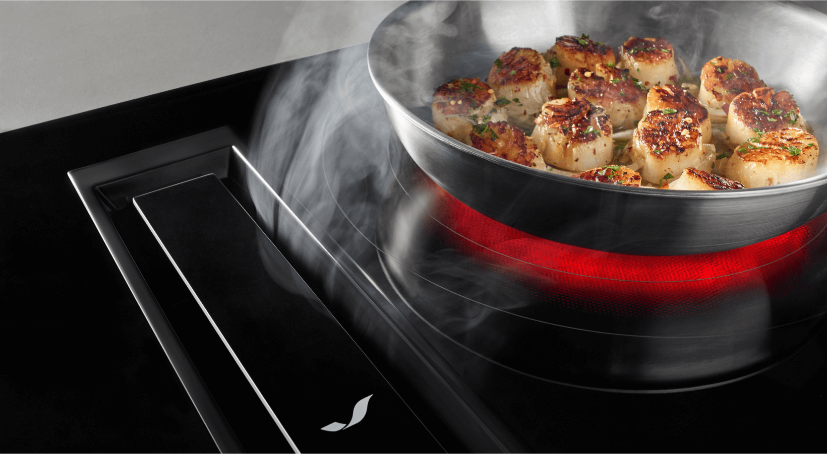 Modern downdraft range and oven combination unit showcased in a clean kitchen setup with scallops in a pan.