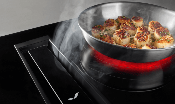 Modern downdraft range and oven combination unit showcased in a clean kitchen setup with scallops in a pan.