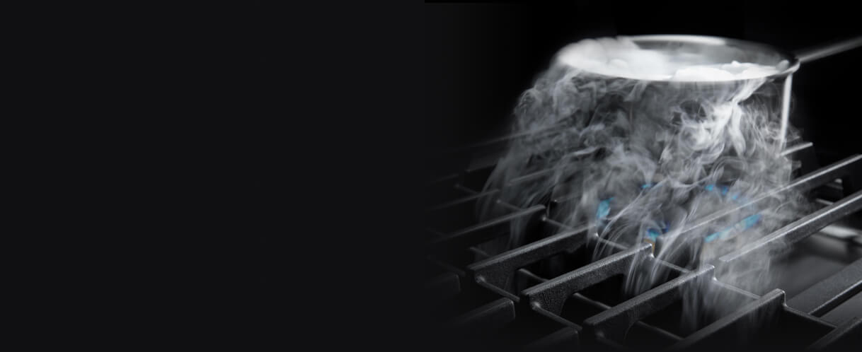 De la vapeur s'échappant d'une casserole aspirée vers le bas par la ventilation à évacuation descendante d'une table de cuisson au gaz.