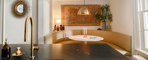 Une cuisine avec une banquette et une table. Deux bougies sont posées sur la table. Au premier plan se trouve un robinet doré.