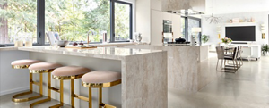 A kitchen with marble counters with four stools.  In the distance is a dining room table with chairs and a mounted TV. 