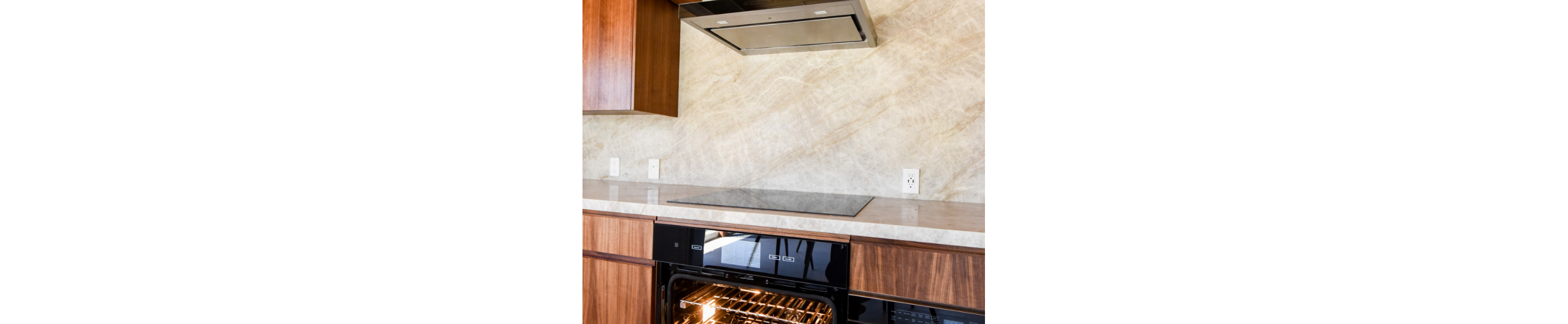 A kitchen with a JennAir Ceramic Cooktop below a JennAir Over-the-Range Hood Vent. Below the cooktop is a JennAir Oven with the door open.