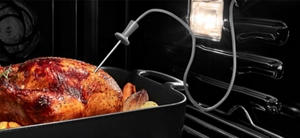 À l’intérieur d’un four encastré JennAir, un poulet entier cuit sur un plateau de rôtissage avec le thermomètre du four inséré.